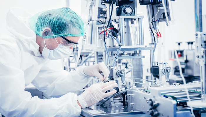A medical lab professional wearing proper PPE as they inspect and perfect a prototype with machining around them.