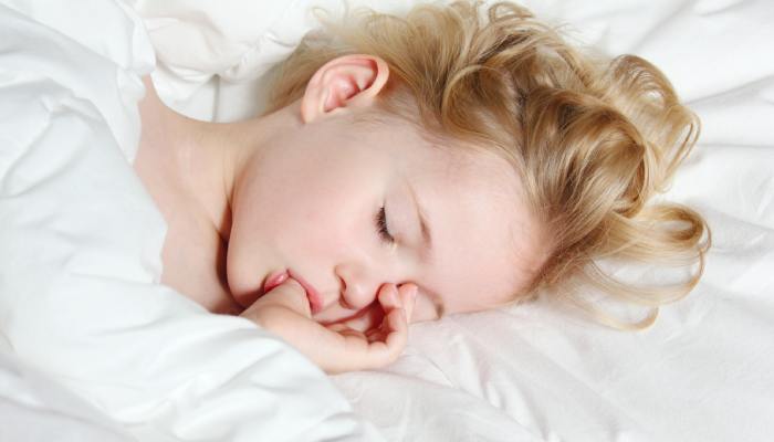 A close-up shows a small child sleeping on a white sheet, sucking their thumb. A white blanket covers the child.