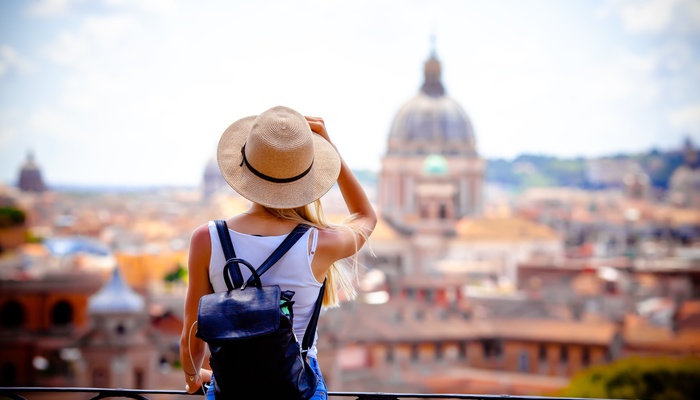 A woman stands on a balcony overlooking the city of Rome, Italy, during the daytime. She wears a backpack.