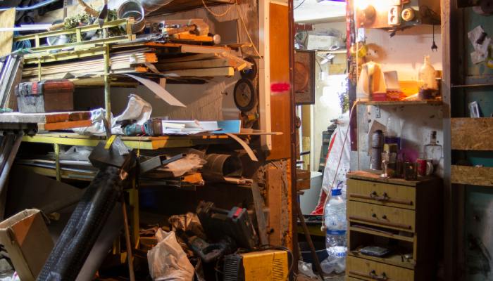 An extremely cluttered garage space, filled with materials and objects balancing on shelves and leaning against walls.