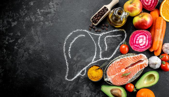 A chalk drawing of a liver on a chalkboard, with various foods, spices, and oils arranged around it.
