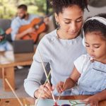 Home 4 A mother and daughter work on a painting in the foreground. A father and son play guitars in the background.