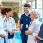 A group of various-aged medical professionals standing in a hospital corridor and smiling at one another.