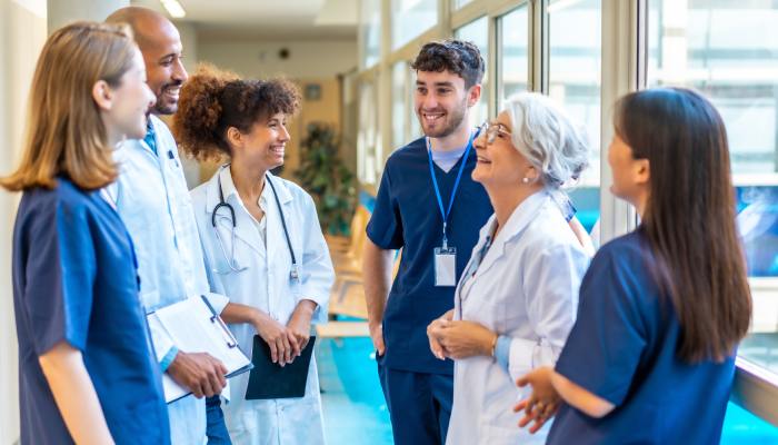 A group of various-aged medical professionals standing in a hospital corridor and smiling at one another.
