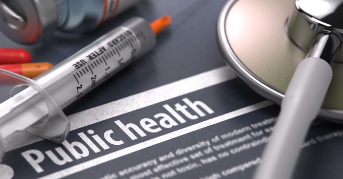 A close-up of a piece of paper that says 'public health' in all caps next to a stethoscope and needle.