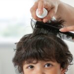 Home 4 A close-up of a child's head with a person off-screen combing through his black hair and holding a product bottle up to spray it.