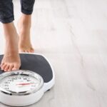 A close-up on a person's feet as they step onto a black-and-white scale with a red marker to indicate the measurement.
