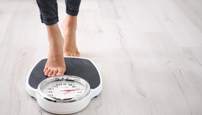 A close-up on a person's feet as they step onto a black-and-white scale with a red marker to indicate the measurement.